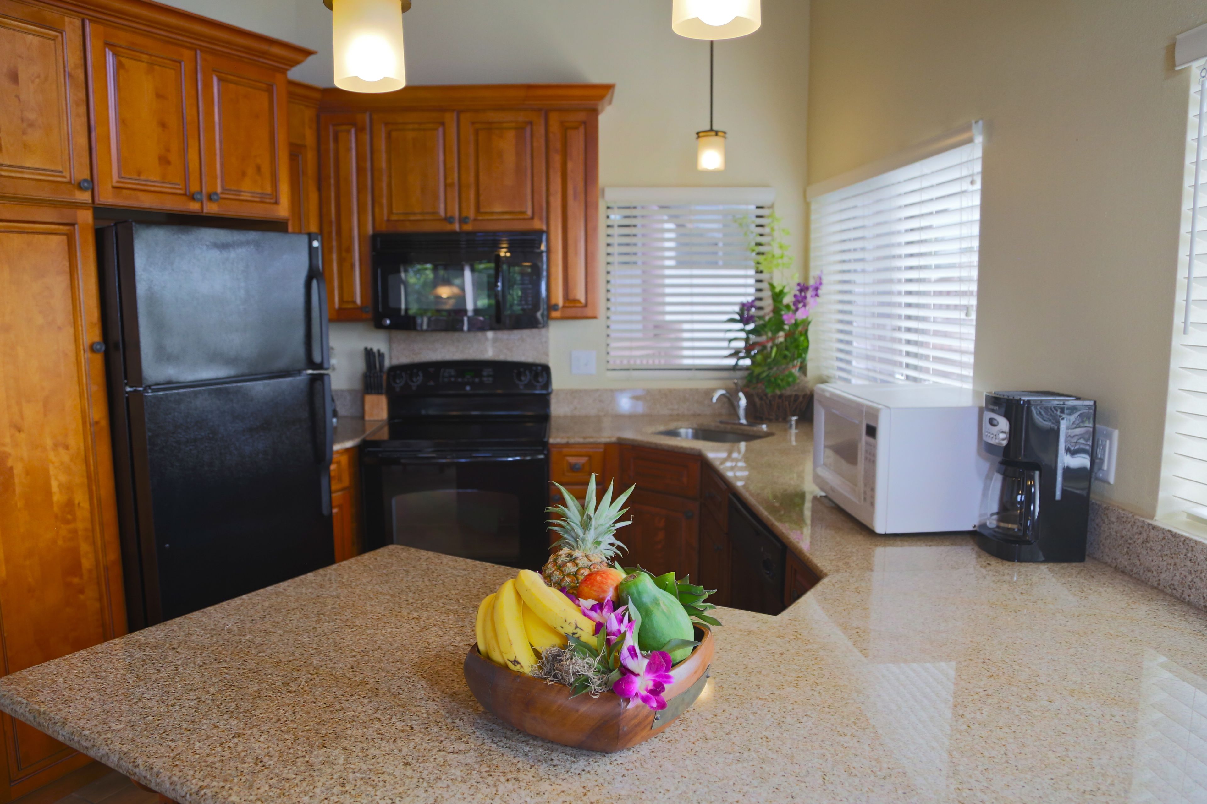 A kitchen with wooden cabinets, a black refrigerator, a microwave, a stove, a coffee maker, and a fruit bowl on the counter.