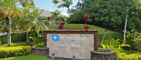 En skylt för Wyndham Ka'Eo Kai, en semesteranläggning där man kan köpa rättigheter till en lägenhet, med en stenmur, frodig grönska och palmer.
