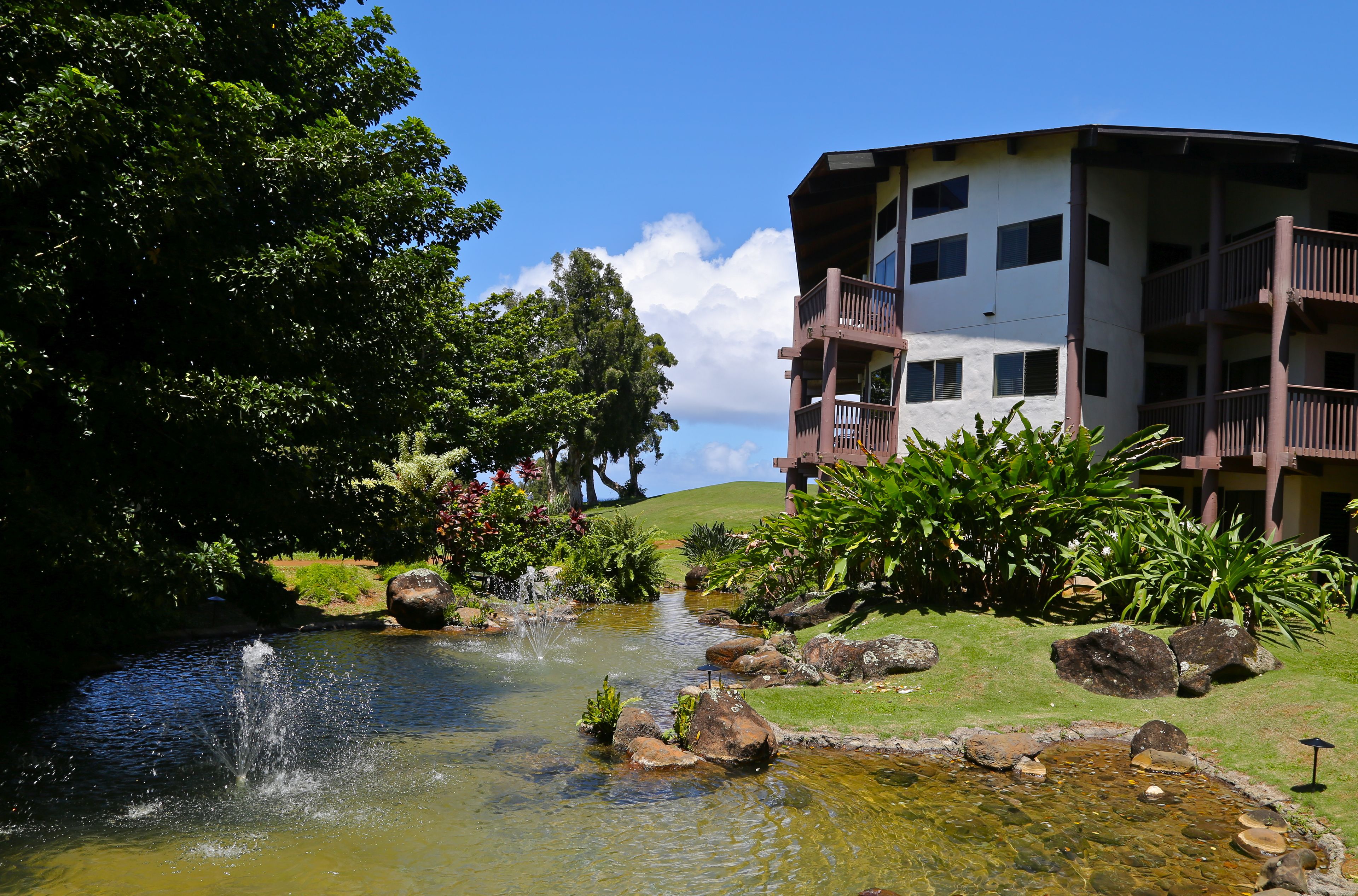 Ein Hotel mit Poolbereich, umgeben von üppiger Vegetation und blauem Himmel.