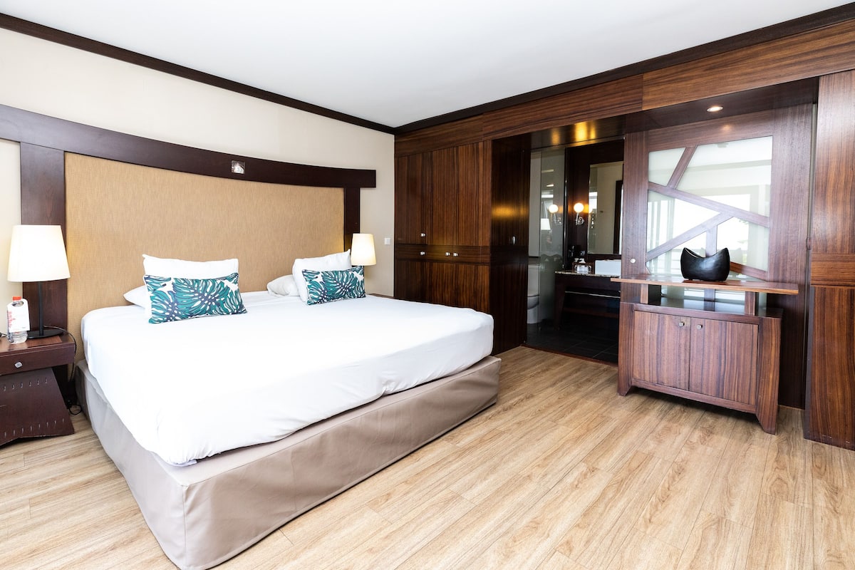Ein Hotelzimmer mit einem großen Bett, einem hölzernen Kopfteil und einem Schrank mit Spiegel.