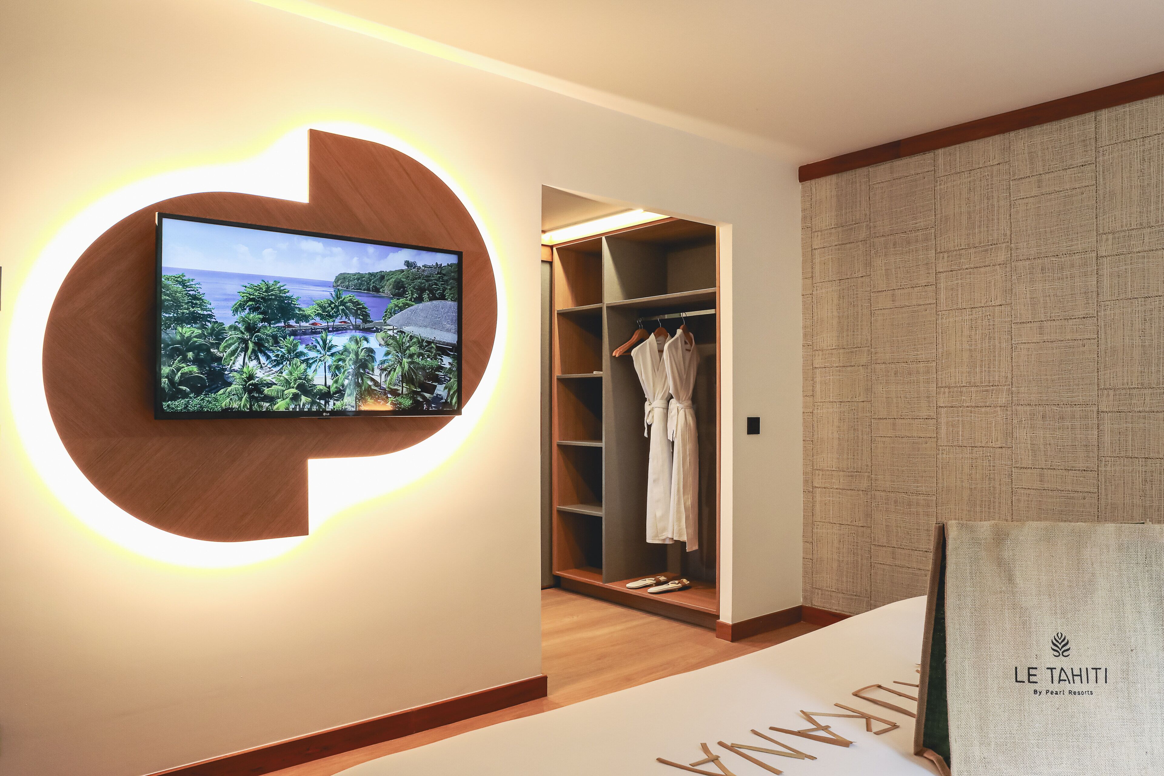 A hotel room with a TV mounted on a wall, a walk-in closet with hanging robes, and a bed with a large pillow.