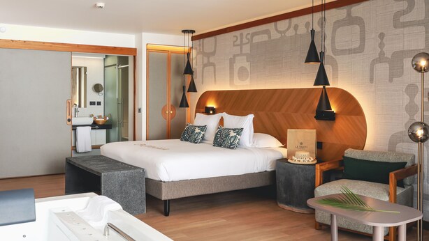 A modern hotel room with a large bed, a sitting area with a small table, a bathtub, and a large mirror. - Tahiti Pearl Beach Resort (Arue)