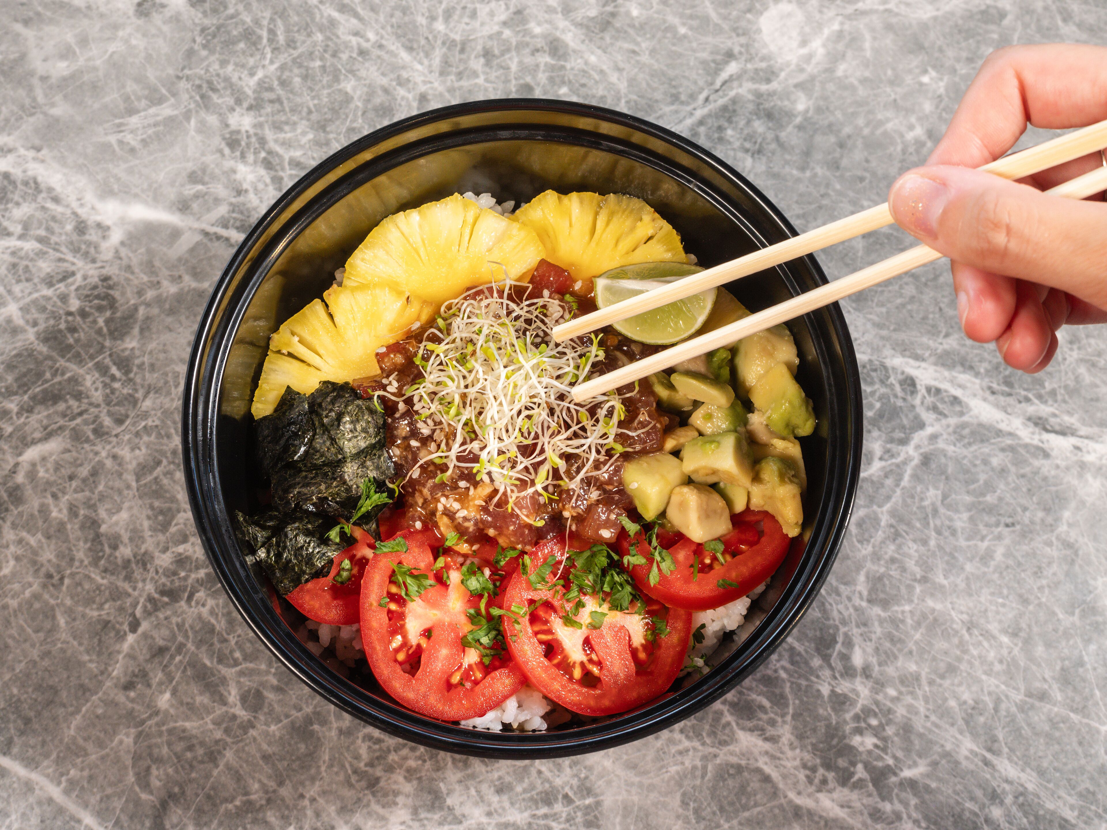 A bowl of food with chopsticks, containing rice, avocado, tomato, and other ingredients.