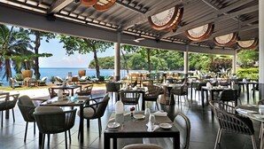 An outdoor dining area with tables and chairs, overlooking a beach and ocean. - Tahiti Pearl Beach Resort (Arue)
