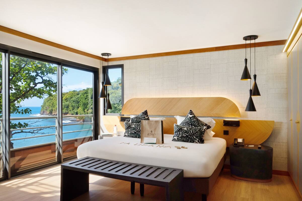 Ein modernes Schlafzimmer mit einem großen Bett, einem Holzkopfteil und Meerblick.