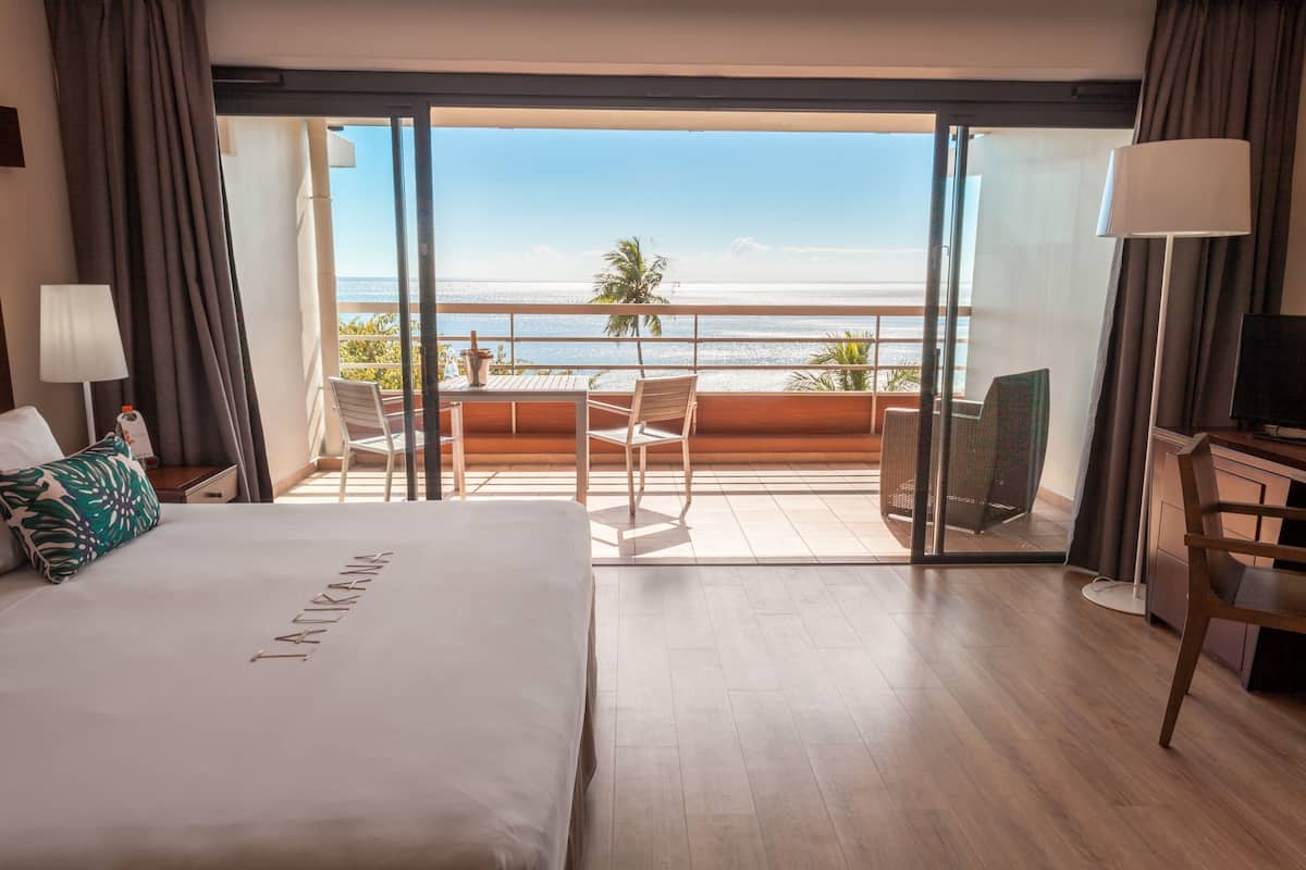 Ein Hotelzimmer mit Bett, Schreibtisch, Stuhl und einem Balkon mit Blick auf Strand und Meer.