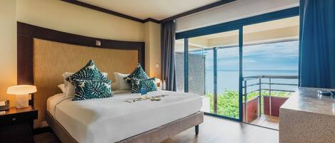 A hotel room with a large bed, a nightstand, a desk, and a balcony with a view.