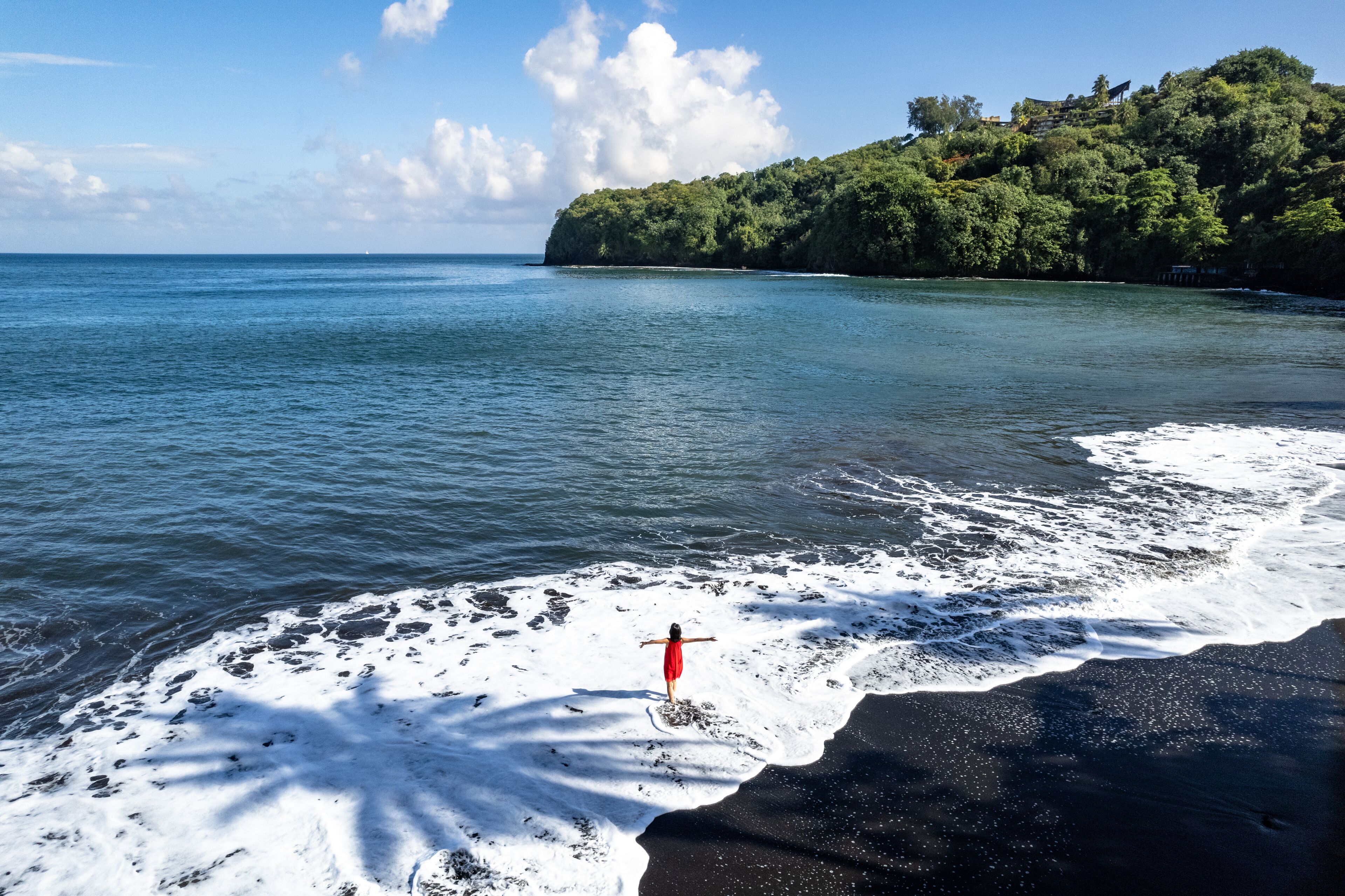 A beach with a red marker, calm sea, and a forested hill in the background.