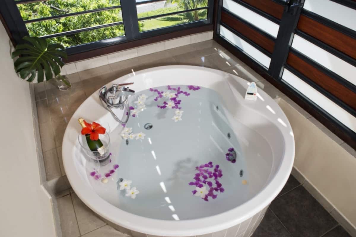 Ein modernes Badezimmer mit freistehender Badewanne, einer Glasvase mit Blumen und Blick ins Grüne durch ein Fenster.