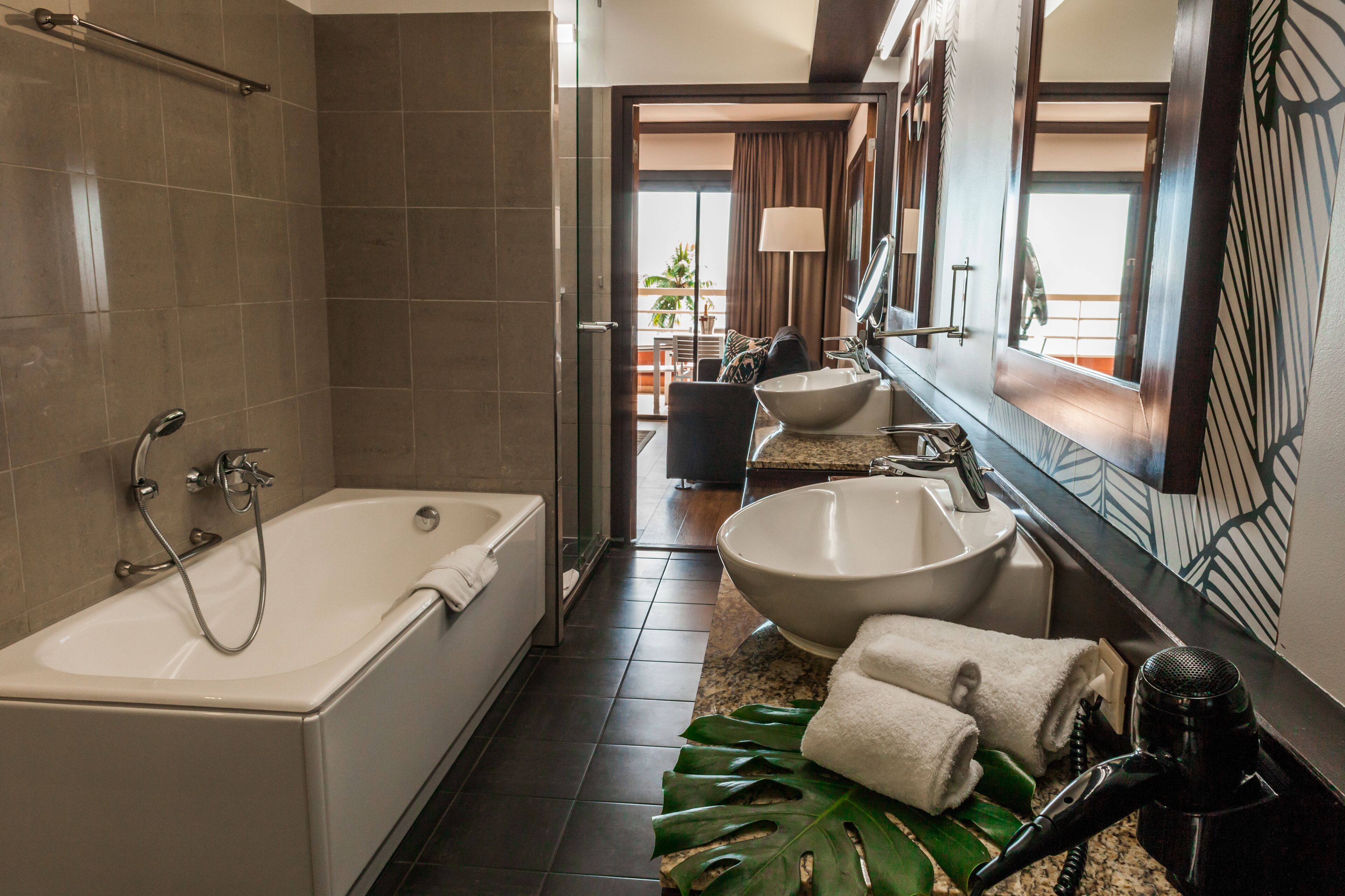 A modern bathroom with a bathtub, two sinks, and a large mirror.