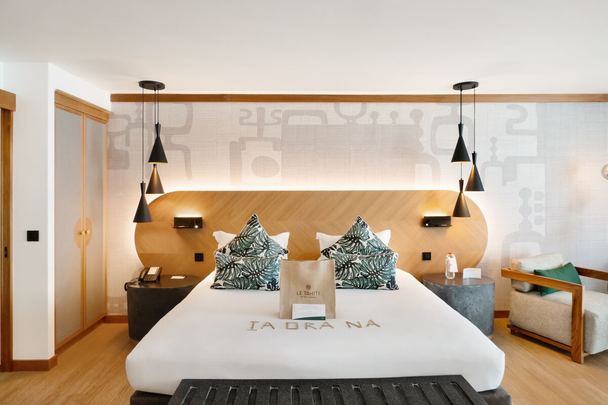 Habitación de hotel moderna con una cama grande, dos mesitas de noche, una lámpara auxiliar y un cabecero de madera, además de lámparas colgantes.