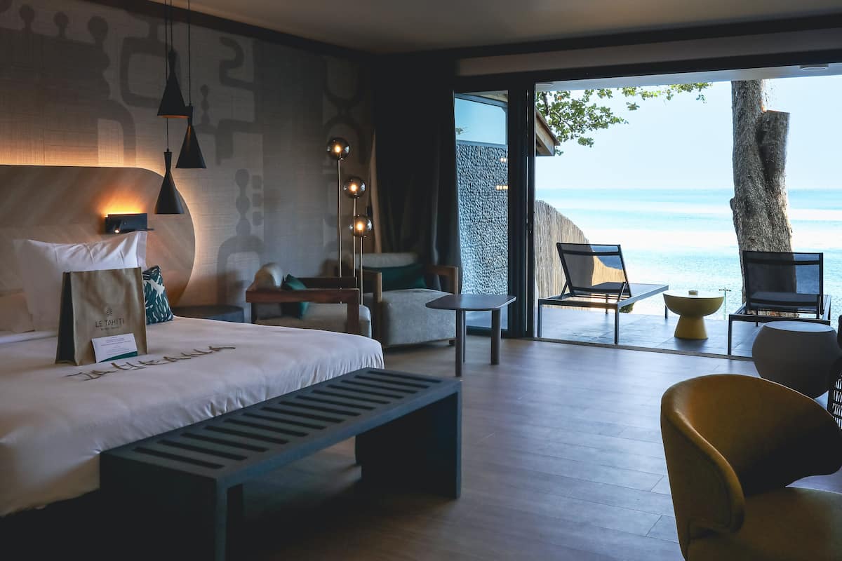 Ein modernes Hotelzimmer mit einem großen Bett, einer Bank, einem Schreibtisch und Blick auf das Meer.