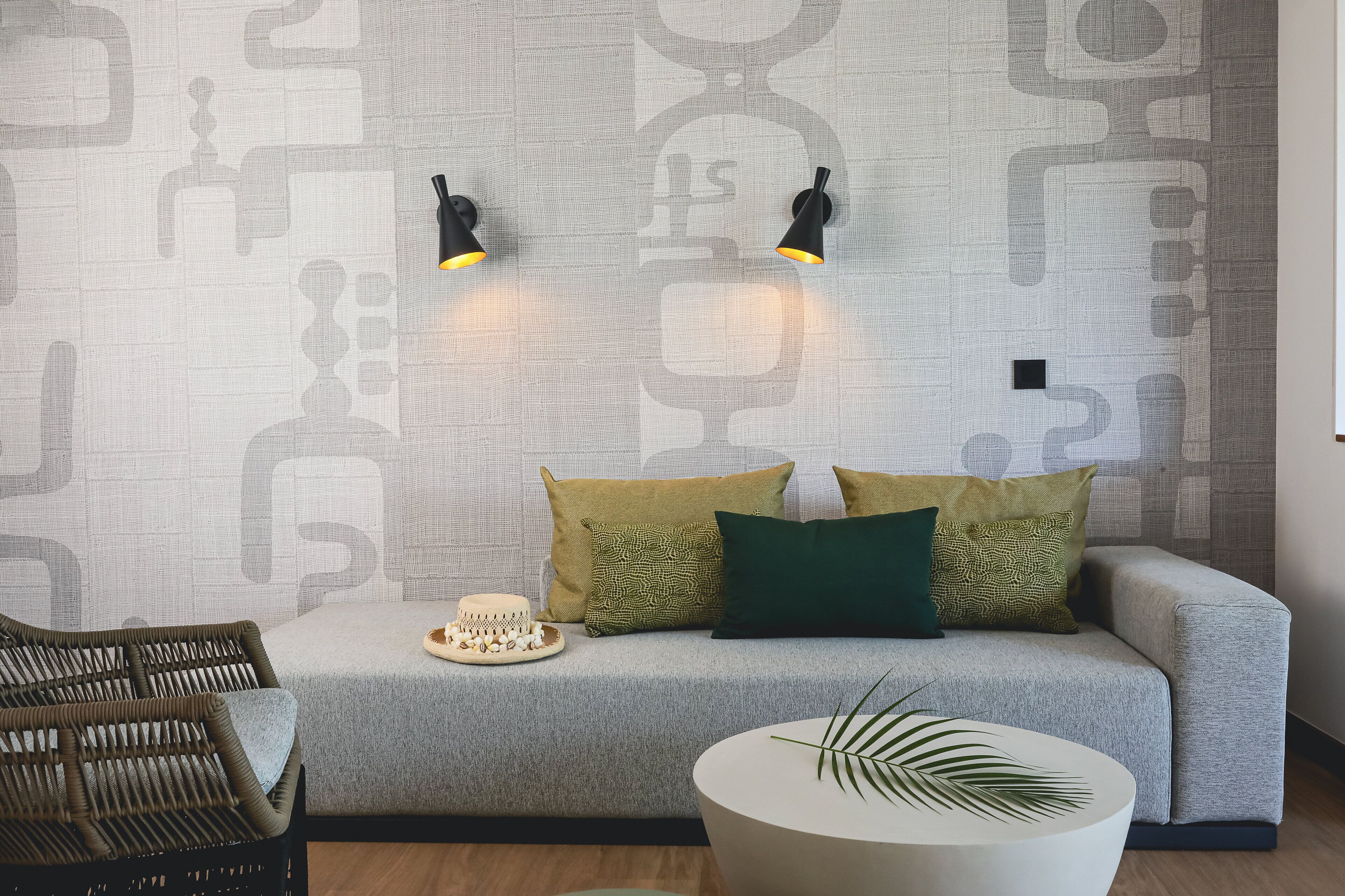 A modern living room with a grey sofa, two black wall sconces, and a round white coffee table with a plant.