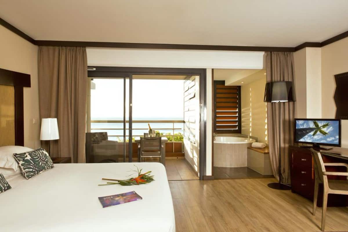 Ein Hotelzimmer mit Bett, Schreibtisch, Fernseher, Bad und einem Balkon mit Aussicht.