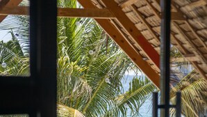 A wooden deck with a thatched roof, overlooking a beach with palm trees and the ocean. - Amami Beach Resort (Puerto Galera)