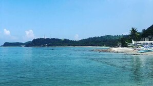 A coastal view with clear turquoise waters, a sandy beach, and a forested hill in the background. - Amami Beach Resort (Puerto Galera)