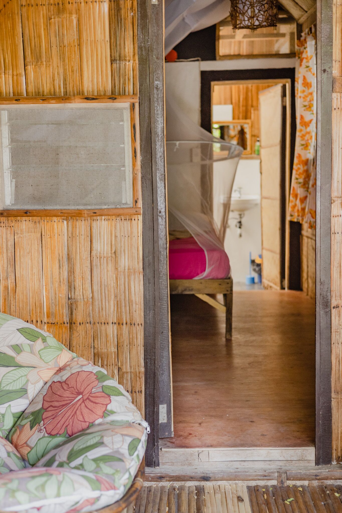 A room with a bed covered by a mosquito net, a wooden wall, and a visible bathroom area.