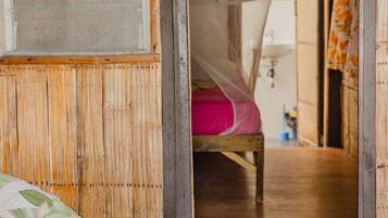 A room with a bed covered by a mosquito net, a wooden wall, and a visible bathroom area.