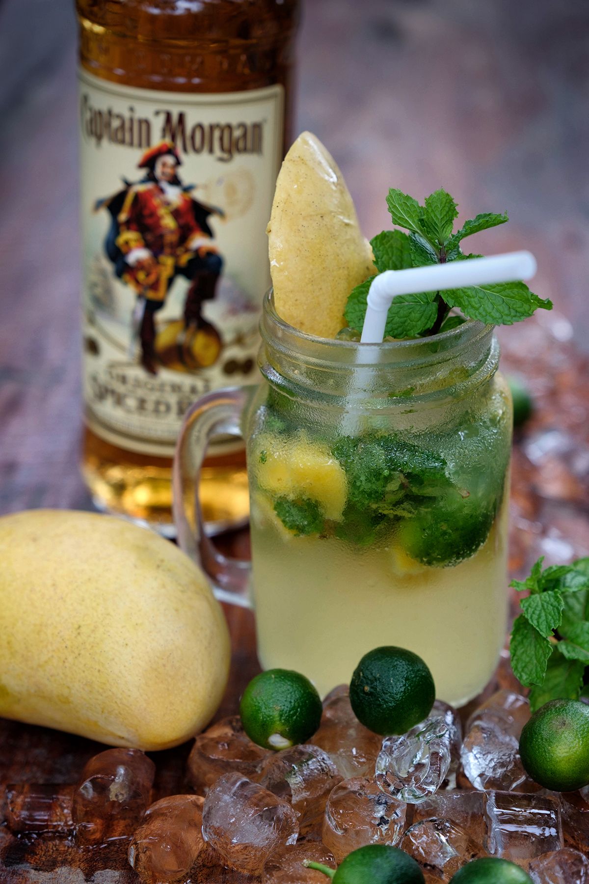 Een drankje met een partje citroen en munt, ijsblokjes, en een fles met de tekst 'Captain Morgan' op de achtergrond.