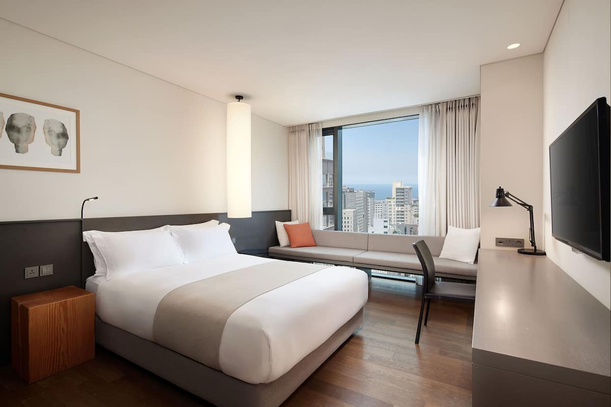 Una habitación de hotel moderna con una cama grande, un sofá, un televisor y una ventana con vistas a la ciudad.