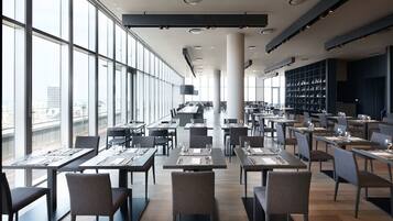 Un espace de restauration moderne, doté de tables et de chaises, de grandes fenêtres et offrant une vue sur la ville.