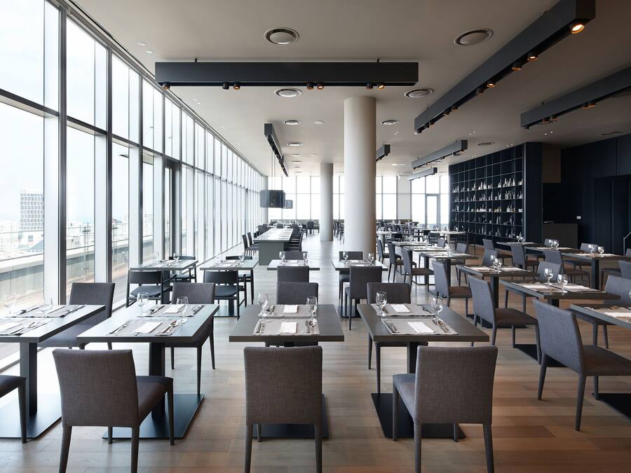 Un espace de restauration moderne, doté de tables et de chaises, de grandes fenêtres et offrant une vue sur la ville.