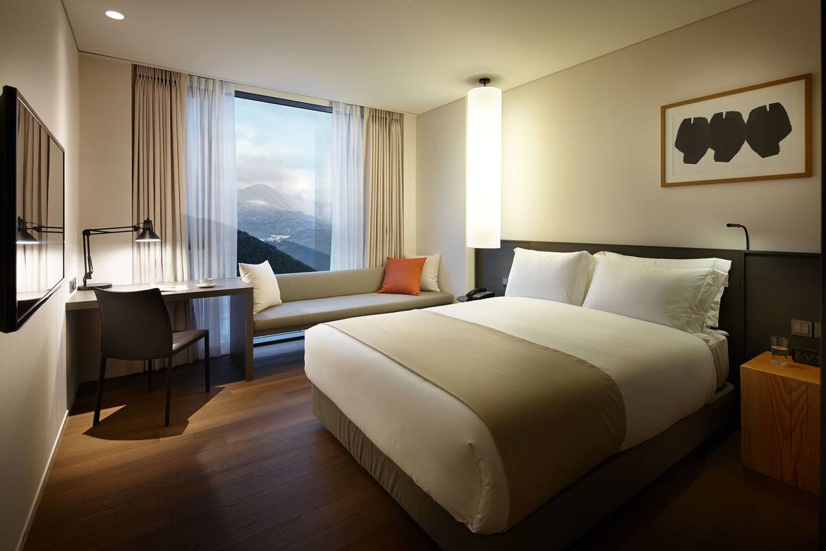 Habitación de hotel con una cama grande, un escritorio con silla, una ventana con cortinas y una obra de arte colgada en la pared.