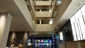 A modern hotel lobby with a high ceiling, glass railings, and a reception desk. - Shilla Stay Jeju Airport (Jeju City)