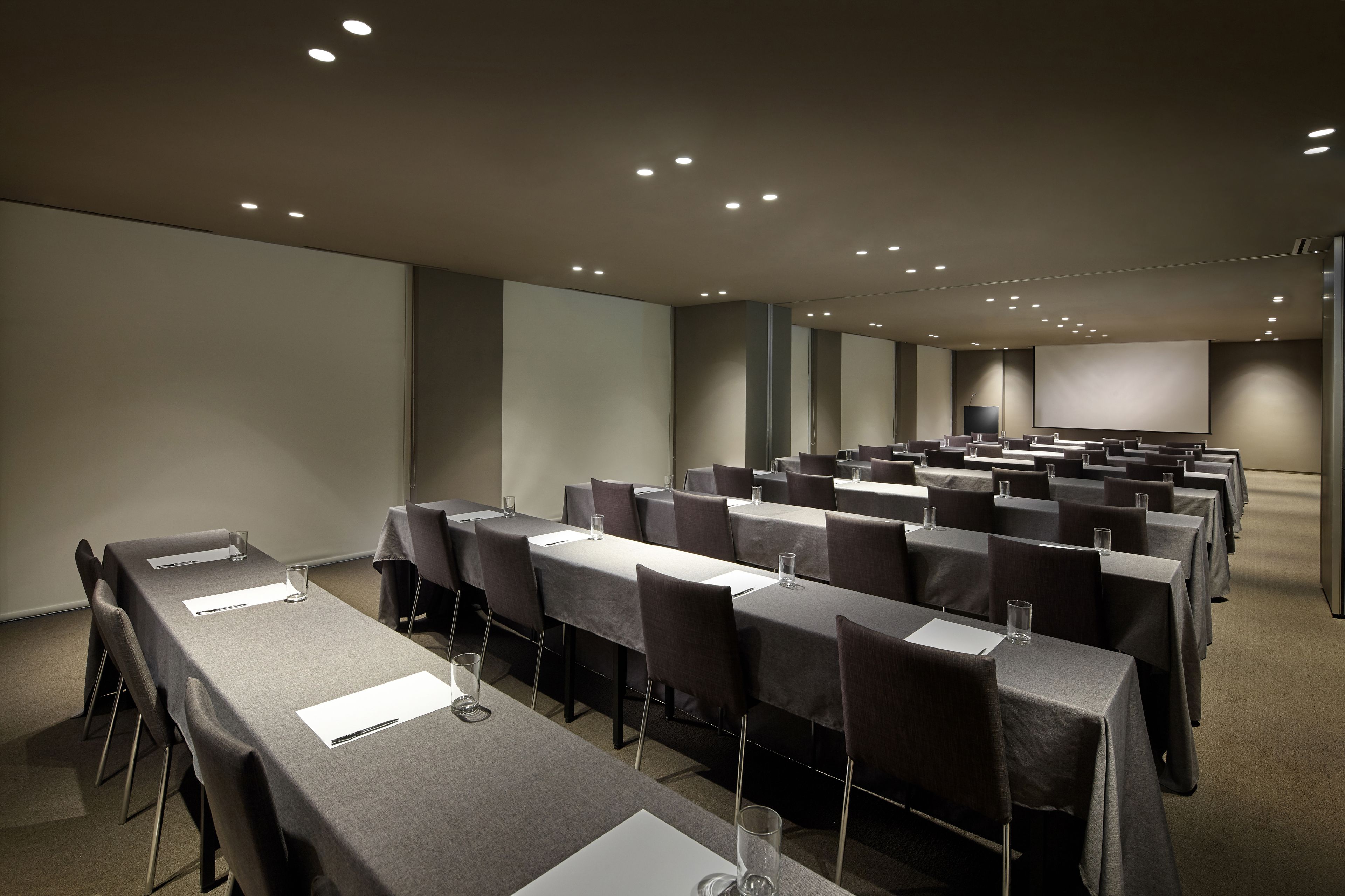A conference room with rows of tables and chairs, equipped with nameplates and glasses.