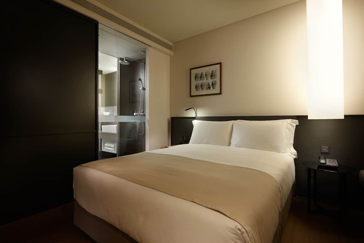 Habitación de hotel con una cama grande, una mesita de noche con lámpara y un cuadro en la pared.