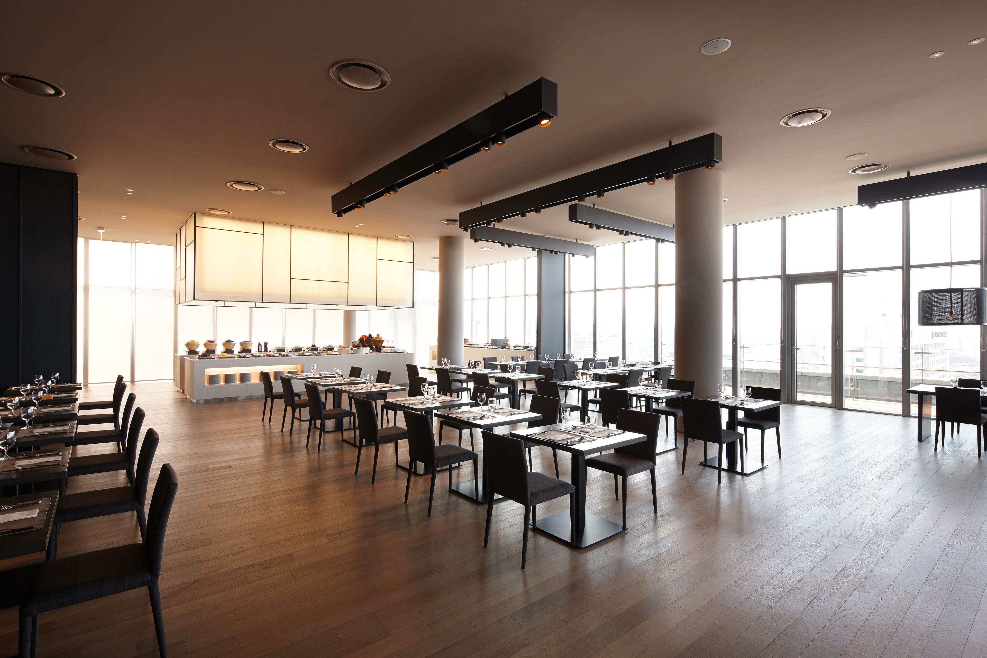 Un vaste espace dédié à la salle à manger, avec de nombreuses tables et chaises, de grandes fenêtres et une cuisine centrale.