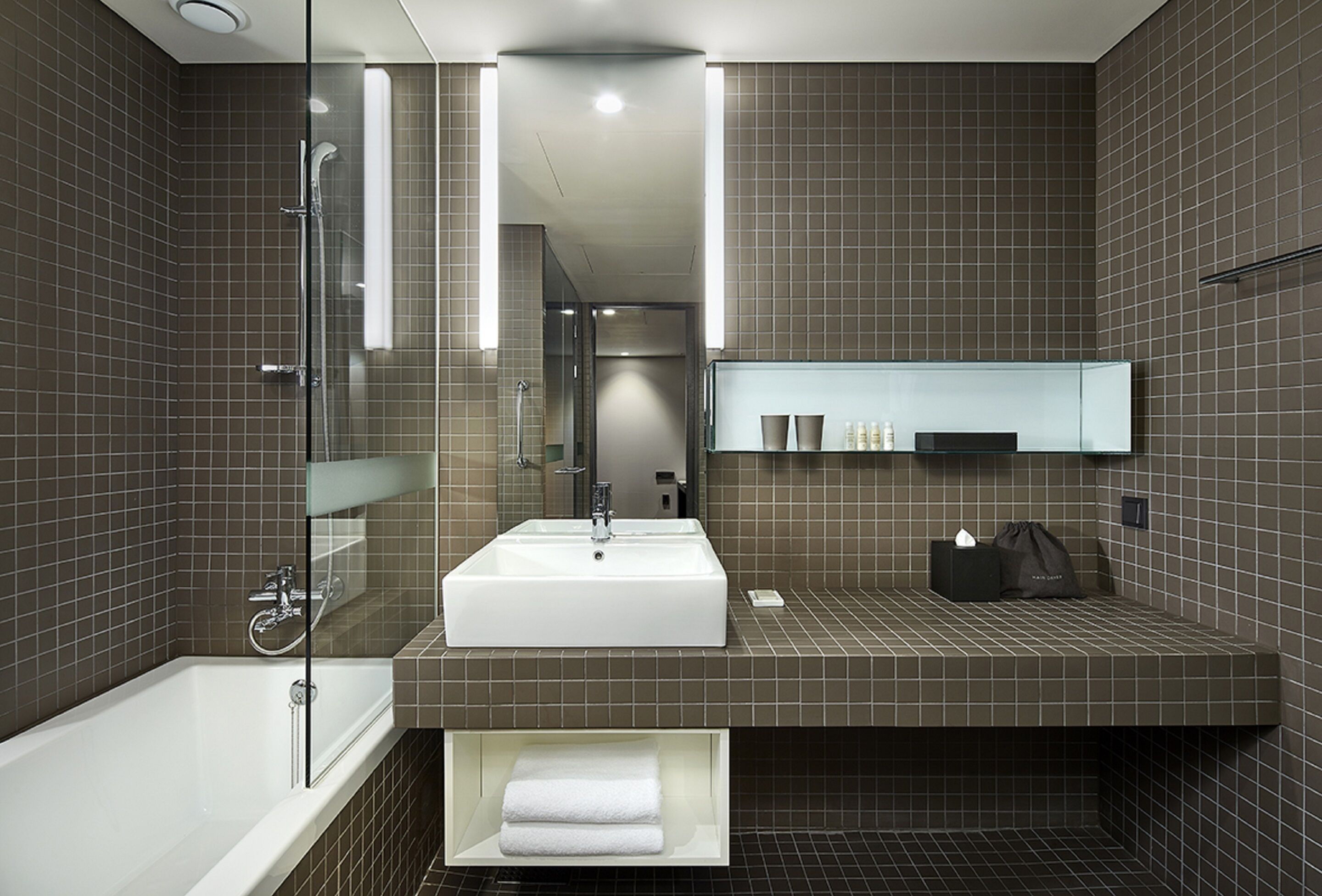 A modern bathroom with a large white sink, a glass-enclosed shower, and a dark tiled wall.