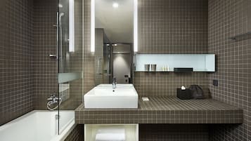 A modern bathroom with a large white sink, a glass-enclosed shower, and a dark tiled wall.
