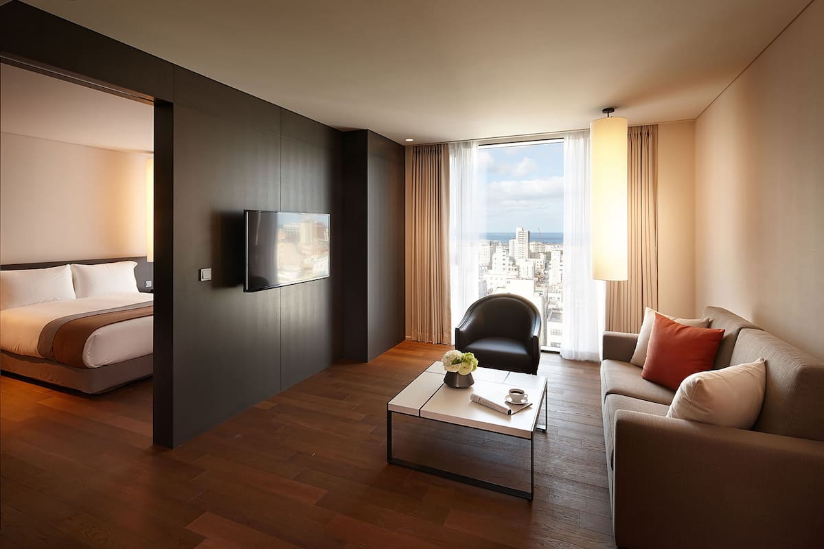 Una habitación de hotel moderna con cama, sofá, mesa de centro y televisor montado en la pared.