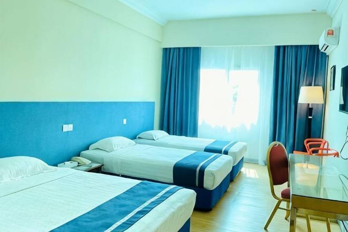 Ein Hotelzimmer mit drei Betten, einem Schreibtisch, einem Stuhl und einem fenster mit Vorhängen.