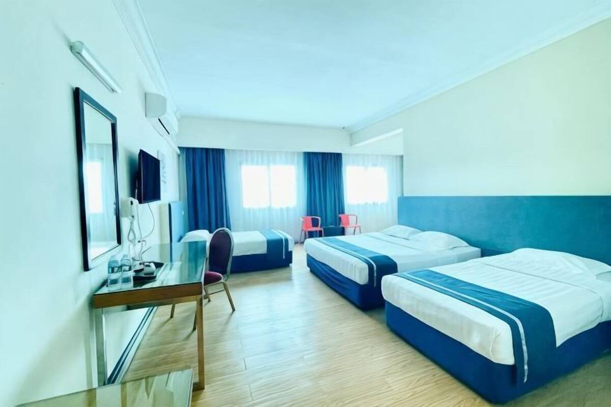 Ein Hotelzimmer mit zwei Betten, einem Schreibtisch, einem Stuhl, einem Fernseher und einem Fenster mit Vorhängen.
