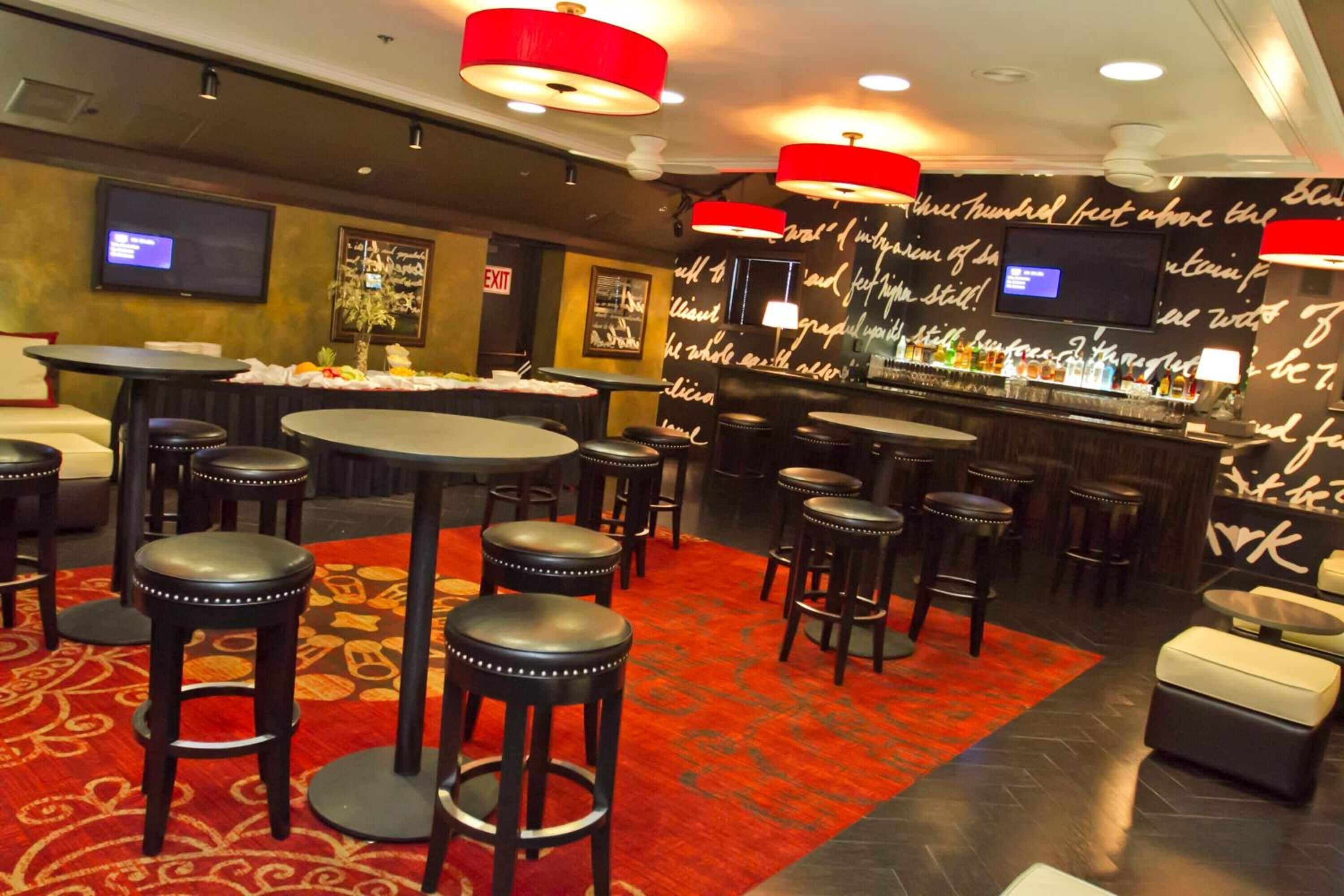 A restaurant with multiple round tables and stools, a red carpet, and a bar area with a black and white patterned wall.