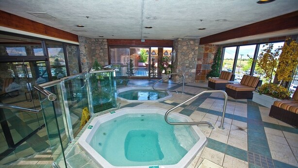 Un área de spa con dos jacuzzis, barandillas de cristal y una zona de estar con vistas al exterior.