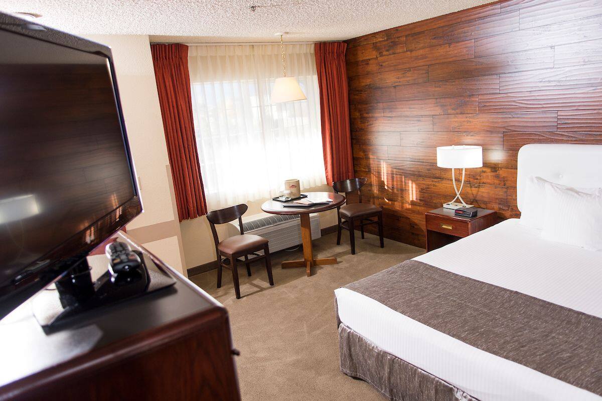 A hotel room with a bed, a TV, a desk with a chair, a lamp, and a window with curtains.
