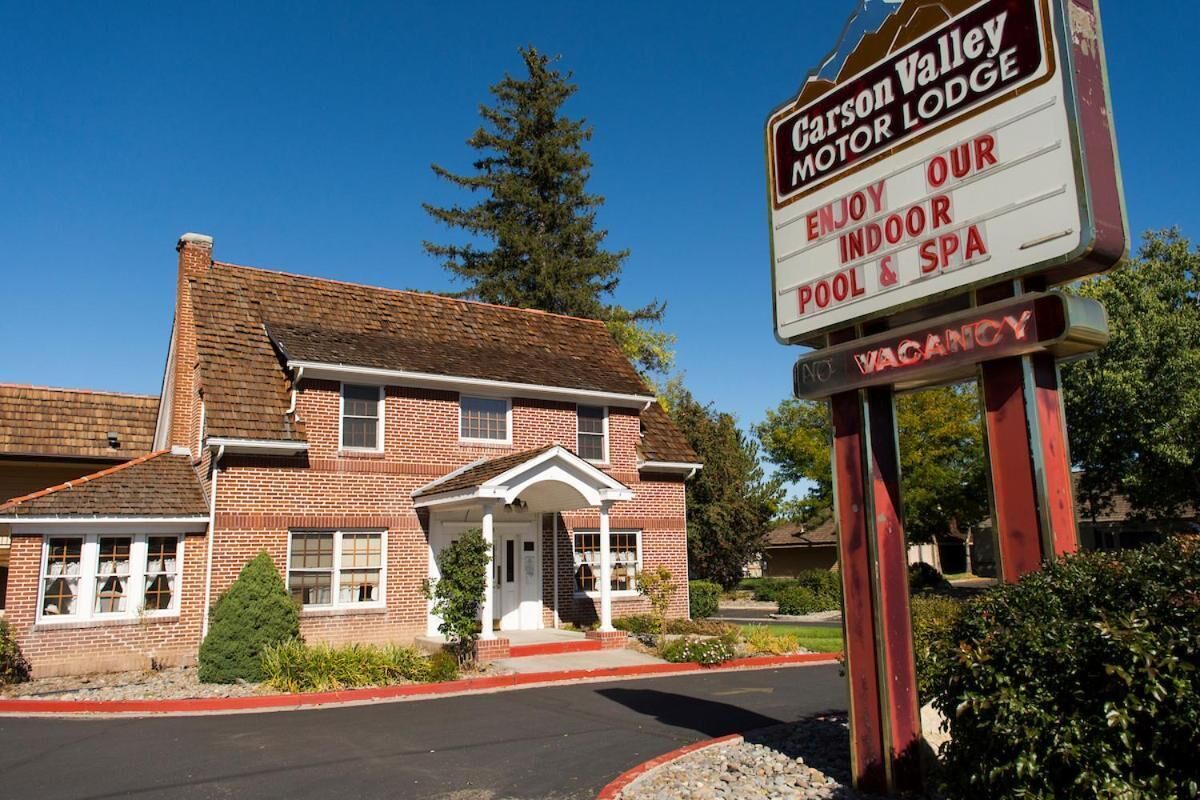 Un Carson Valley Motor Lodge con edificio de ladrillo, entrada cubierta y cartel que indica piscina y spa interior.