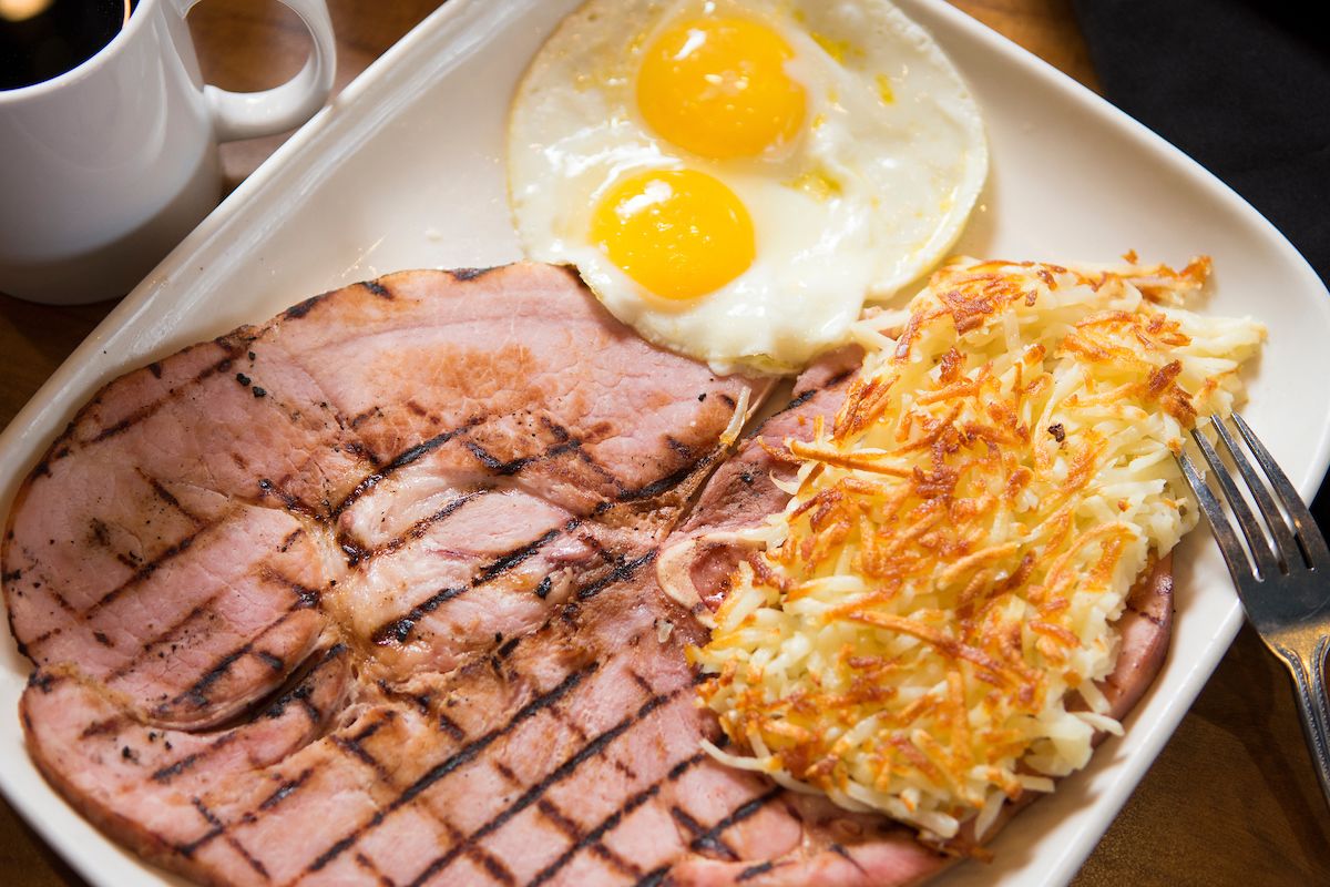 Um prato com presunto grelhado, dois ovos fritos e batata palha.