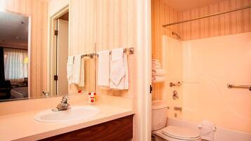 A hotel bathroom with a wooden vanity, a sink, a mirror, a toilet, and a bathtub.