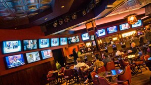 Un bar con varias televisiones mostrando diferentes programas, paneles de madera y sillones de cuero.