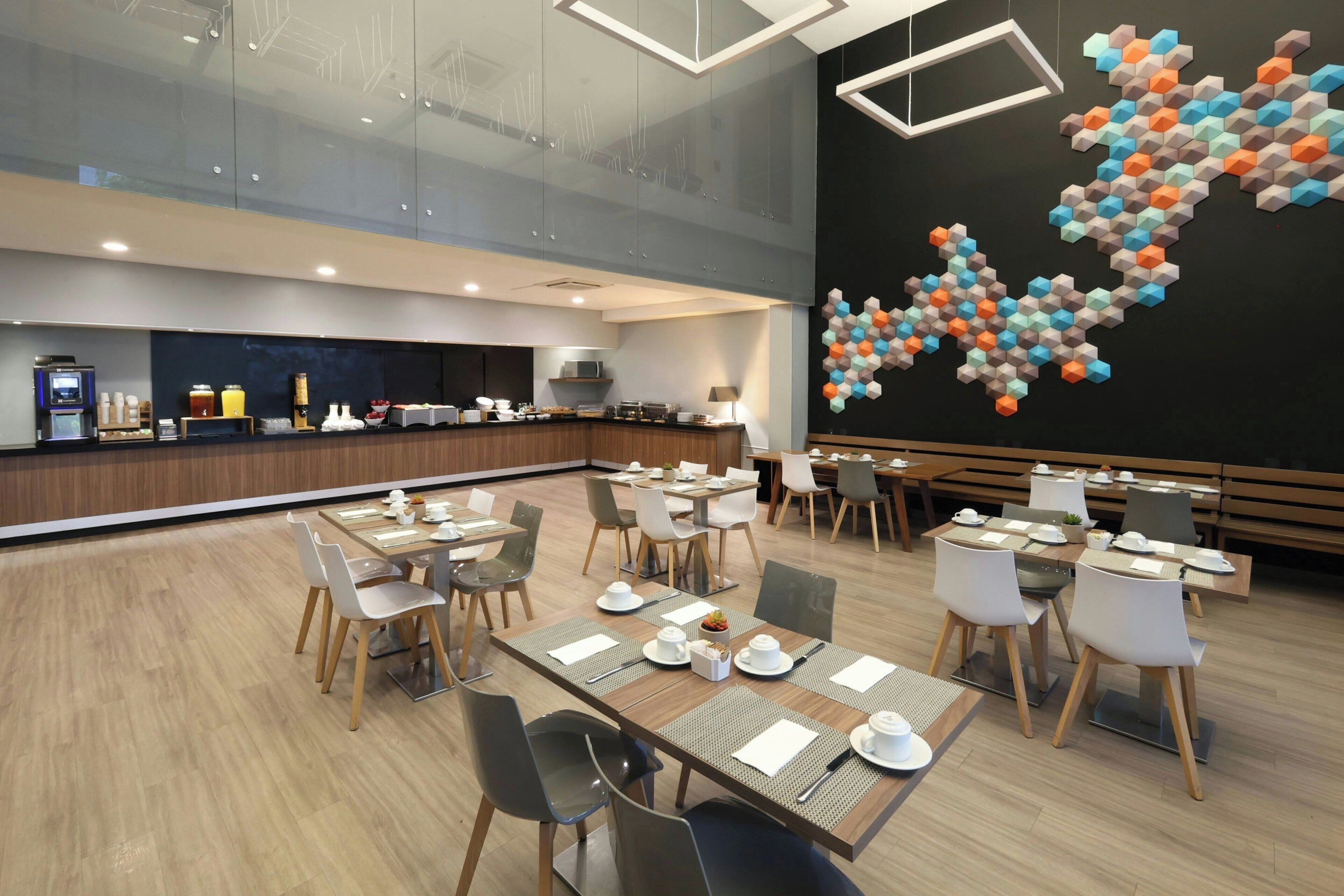 Comedor moderno de hotel con separadores de vidrio, un bufé y una obra de arte geométrica en la pared.