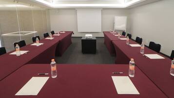 A conference room with long tables, chairs, water bottles, and a projector screen.