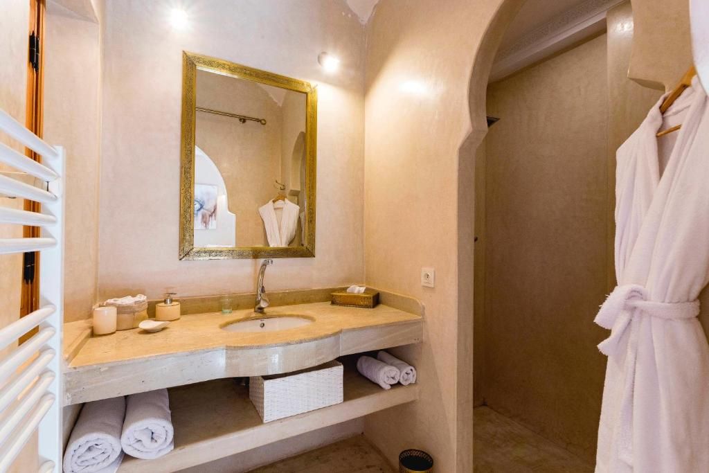 Une salle de bain équipée d’un lavabo, d’un miroir, d’un porte-serviettes et d’un peignoir suspendu.