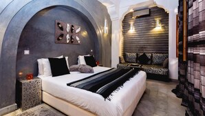 A modern bedroom with a large bed, a seating area, and a unique wall design. - Riad Mazaya (Marrakech)