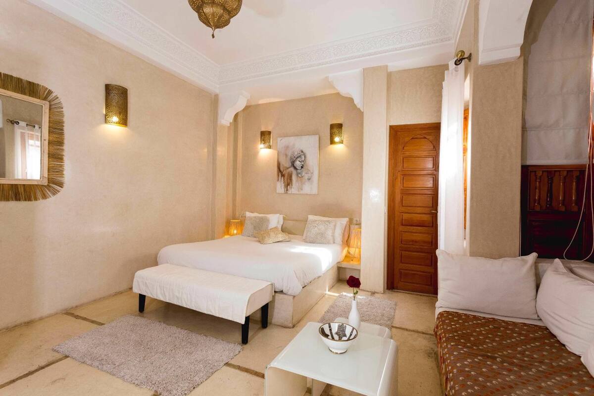Une chambre d  ’hôtel avec un grand lit, une table de chevet ornée d’un vase, une petite table, un miroir et une porte en bois.