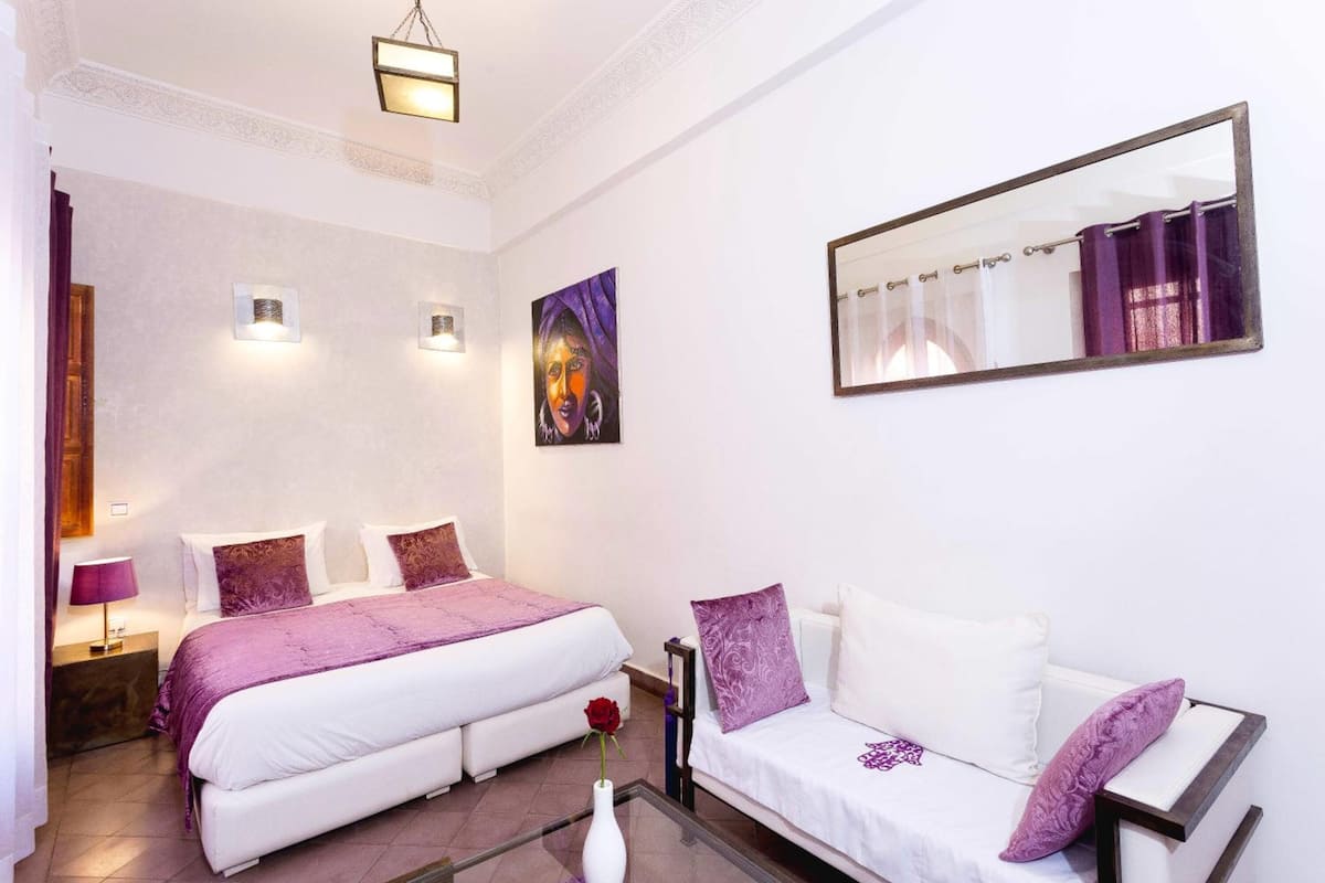 Une chambre à coucher avec un lit, un canapé, un miroir et un tableau accroché au mur.
