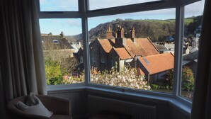 A room with a large window overlooking a village with traditional houses and a hill in the distance. - South View Guest House (Lynton)